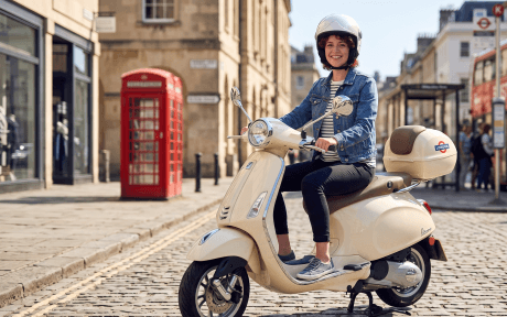 A young urban rider in the UK parking a stylish grey Vespa scooter on a city street, wearing safety gear and carrying a heavy-duty chain lock to highlight affordable and secure moped insurance tips for 2026.
